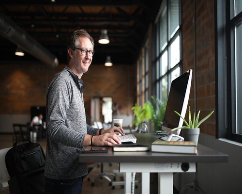 Man stretching his back while standing next to office desk